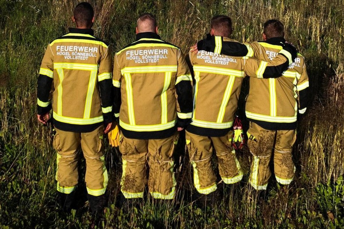 Vier Feuerwehrleute zeigen ihren Rücken und die Aufschrift auf ihren Jacken - dort steht Högel, Sönnebüll, Vollstedt
