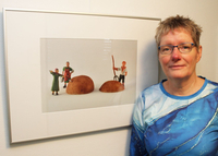 Die Foto-Künstlerin steht neben einem ihrer Bilder. Es heißt Kartoffelernte und zeigt drei Bäuerlich gekleidete Männchen neben einer aufgeschnittenen Kartoffel.