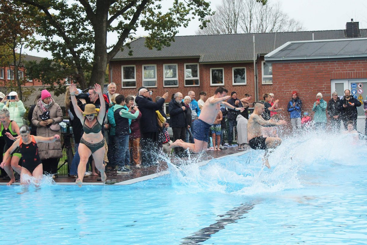 Viele Menschen springen in Badekleidung in ein Wasserbecken