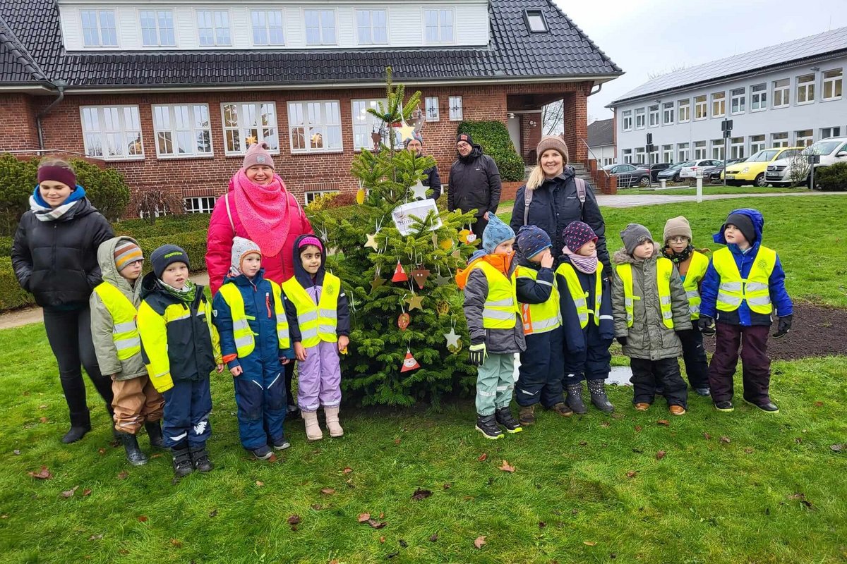 Stolz auf ihr weihnachtliches Werk: die Mädchen und Jungen der Breklumer Kita Hummelhuus. Foto: AMNF eine Gruppe von zehn Kindergartenkindern und einige Erwachsene stehen vor einem geschmückten Weihnachtsbaum