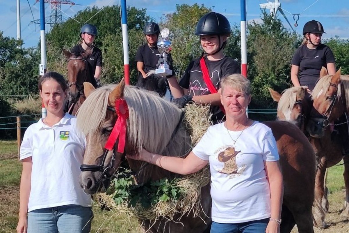 ein Mädchen sitzt auf einem Pferd und hält einen Pokal in der Hand
