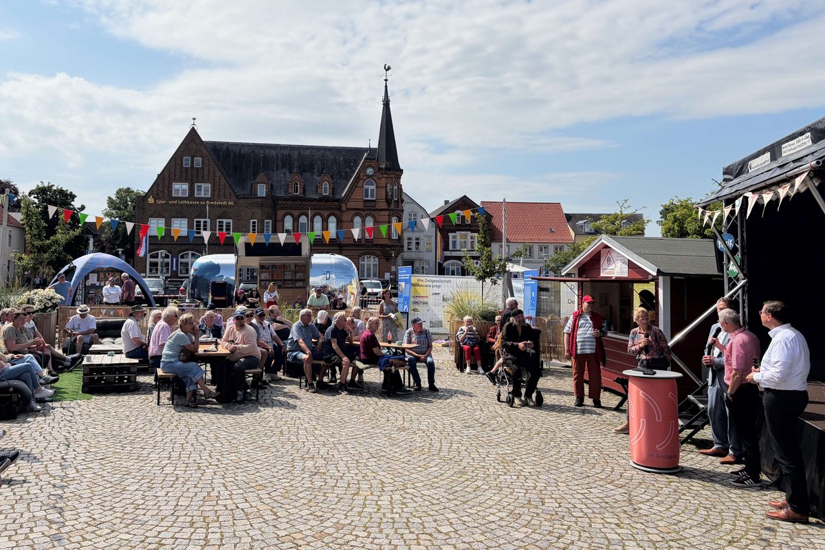 Es war viel los auf dem Marktplatz. Viele Menschen sitzen rund um eine Bühne auf einem Platz